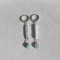 Pair of silver earrings with bar-shaped and round gemstones on a light gray background