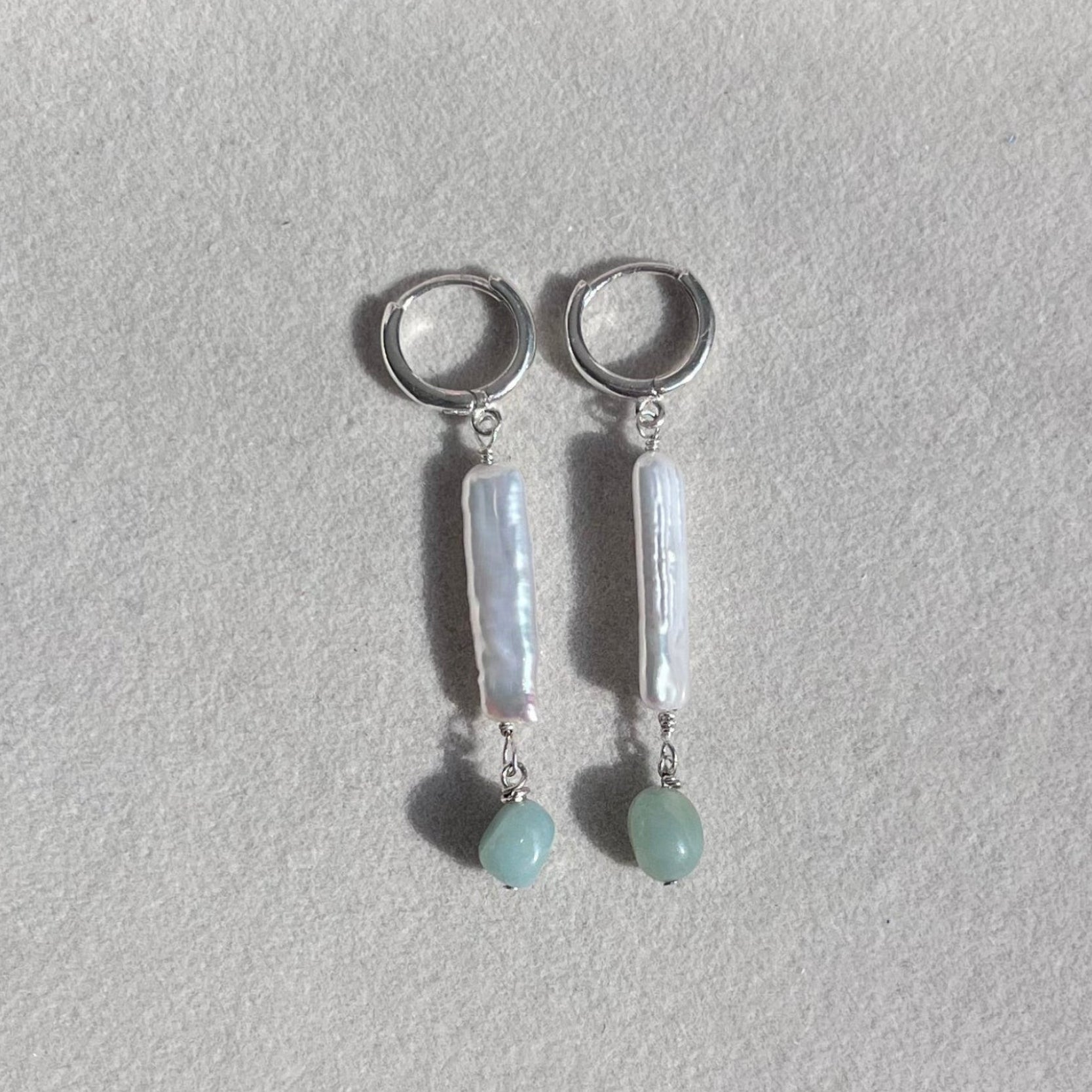 Pair of silver earrings with bar-shaped and round gemstones on a light gray background