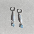 Pair of silver earrings with pearls and blue gemstone drops on a light gray background