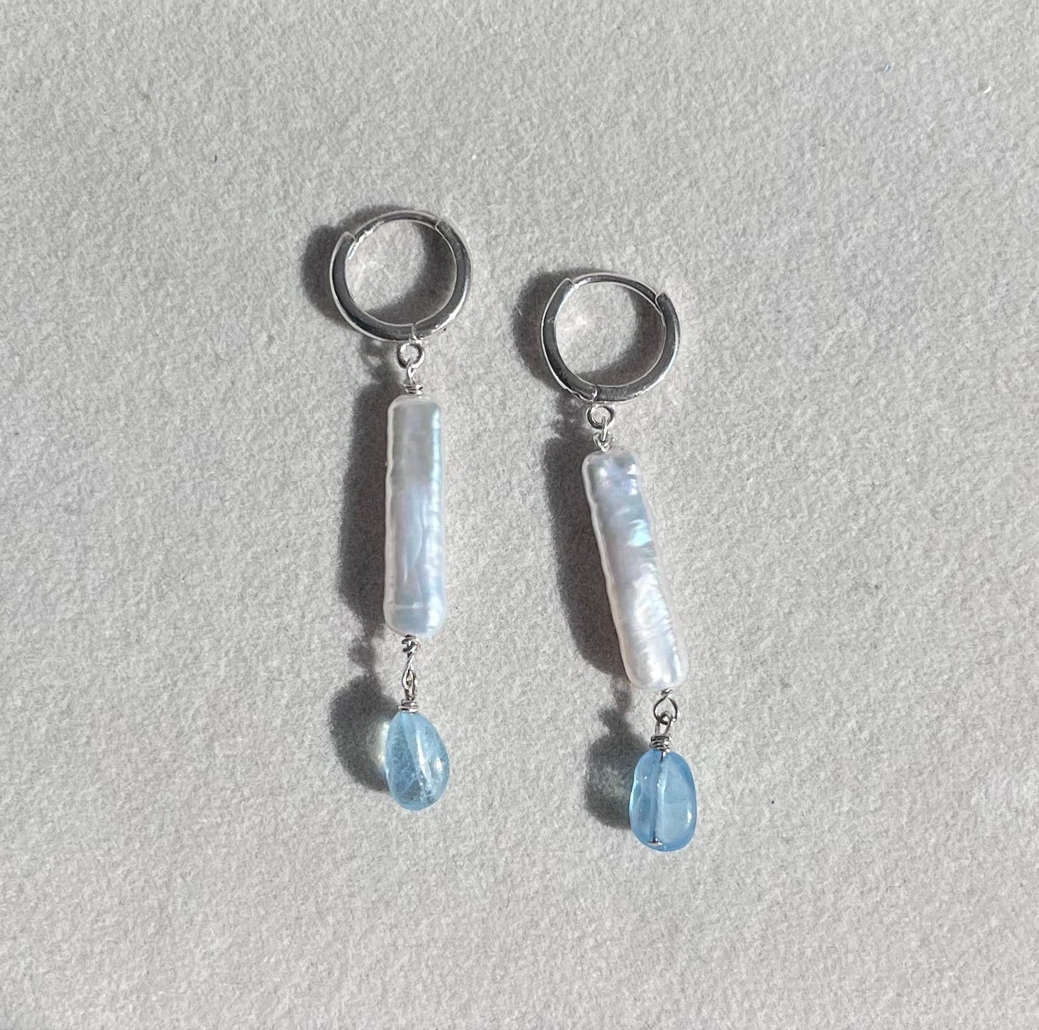 Pair of silver earrings with pearls and blue gemstone drops on a light gray background