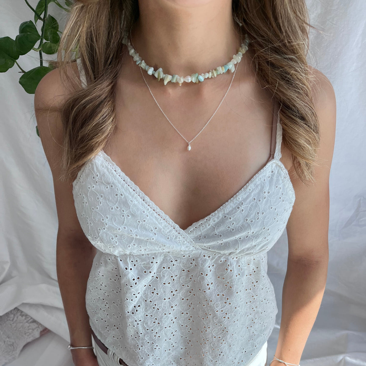 person with white top wearing necklaces
