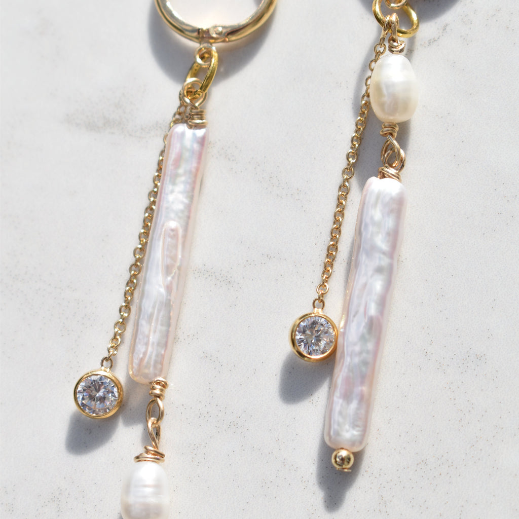 A pair of gold-tone dangle earrings with baroque pearls, clear crystal beads, and small pearl beads, displayed on a light marble surface.