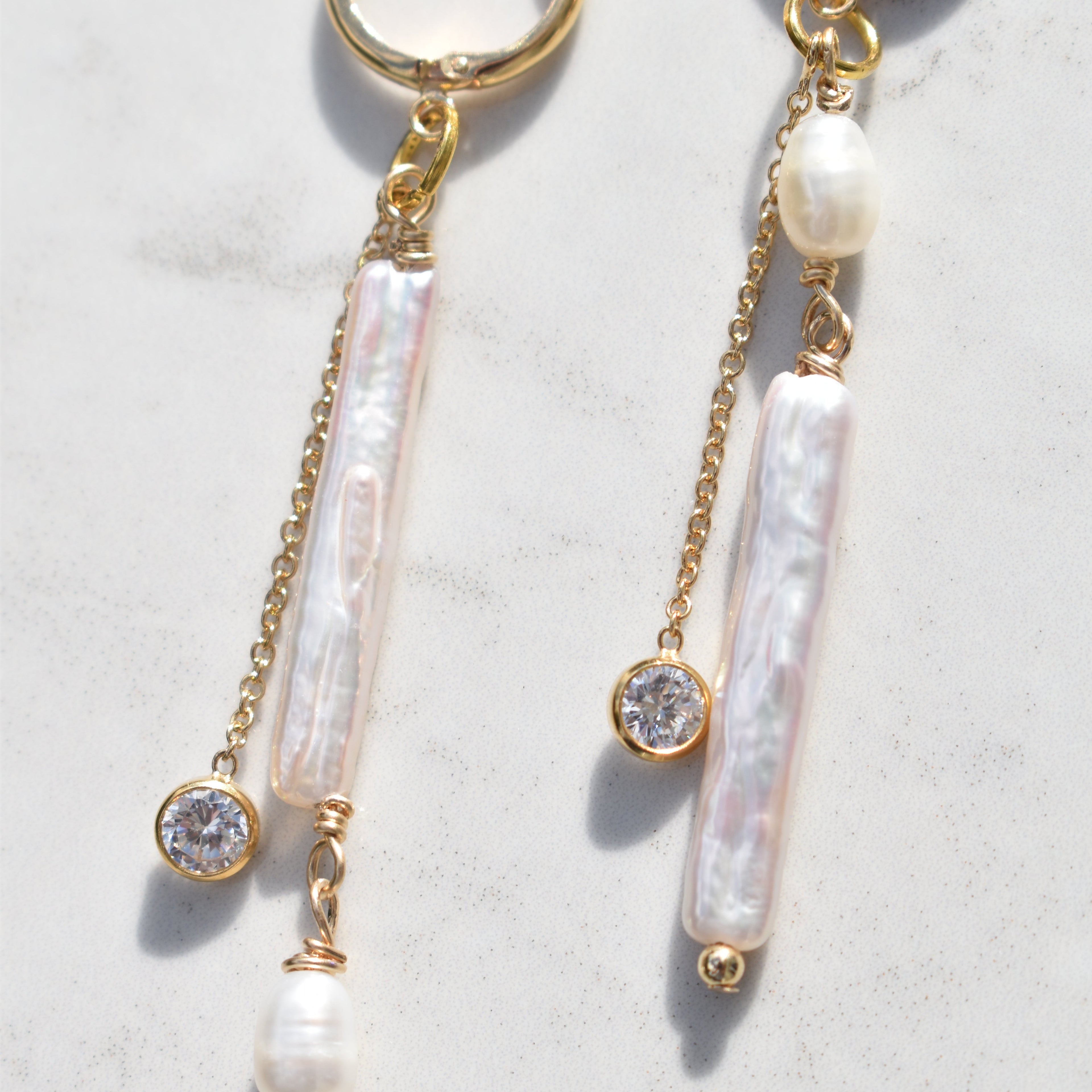 A pair of gold-tone dangle earrings with baroque pearls, clear crystal beads, and small pearl beads, displayed on a light marble surface.