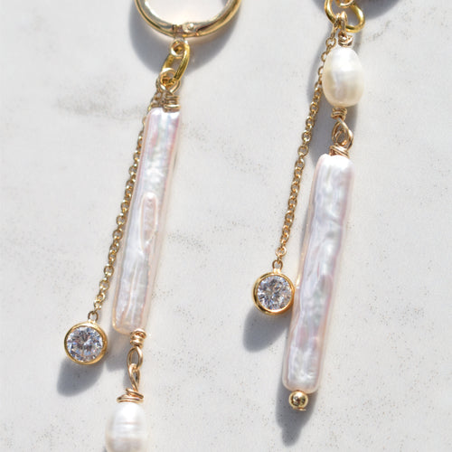 A pair of gold-tone dangle earrings with baroque pearls, clear crystal beads, and small pearl beads, displayed on a light marble surface.