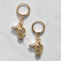 A pair of gold-toned hoop earrings with dangling textured fish charms and small white pearl beads, displayed on a light gray marble surface.