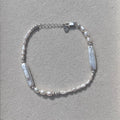 A delicate silver-toned beaded bracelet with two white rectangular inlay elements, displayed inside a light gray jewelry box.