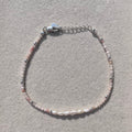 A delicate beaded bracelet with small pink and white beads, silver-toned spacer beads, and a silver lobster clasp, displayed on a textured light gray surface.