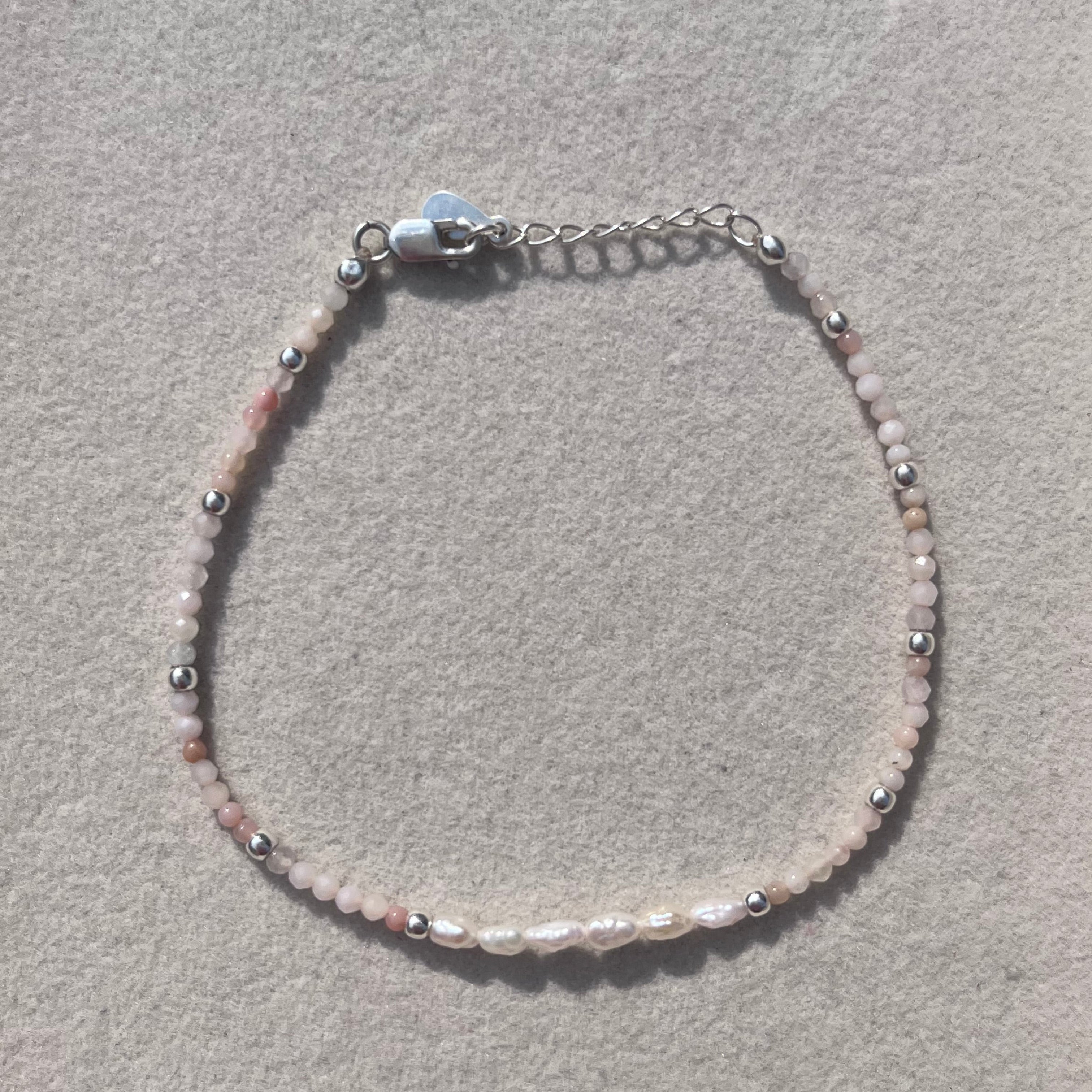 A delicate beaded bracelet with small pink and white beads, silver-toned spacer beads, and a silver lobster clasp, displayed on a textured light gray surface.