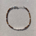 A delicate beaded bracelet with brown tiger's eye beads, silver spacer beads, and a silver clasp, displayed on a textured light gray surface.